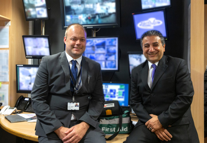 Two men in front of security screens